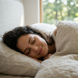 A woman sleeping peacefully on a pillow, wrapped in a light beige linen blanket, enjoying sound sleep from the Deep-Rest Forest Myst Flute formula from Blissthera and Mindscape